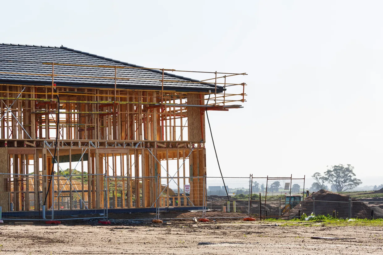 A house under construction with its timber framing exposed and scaffolding standing against the front wall.