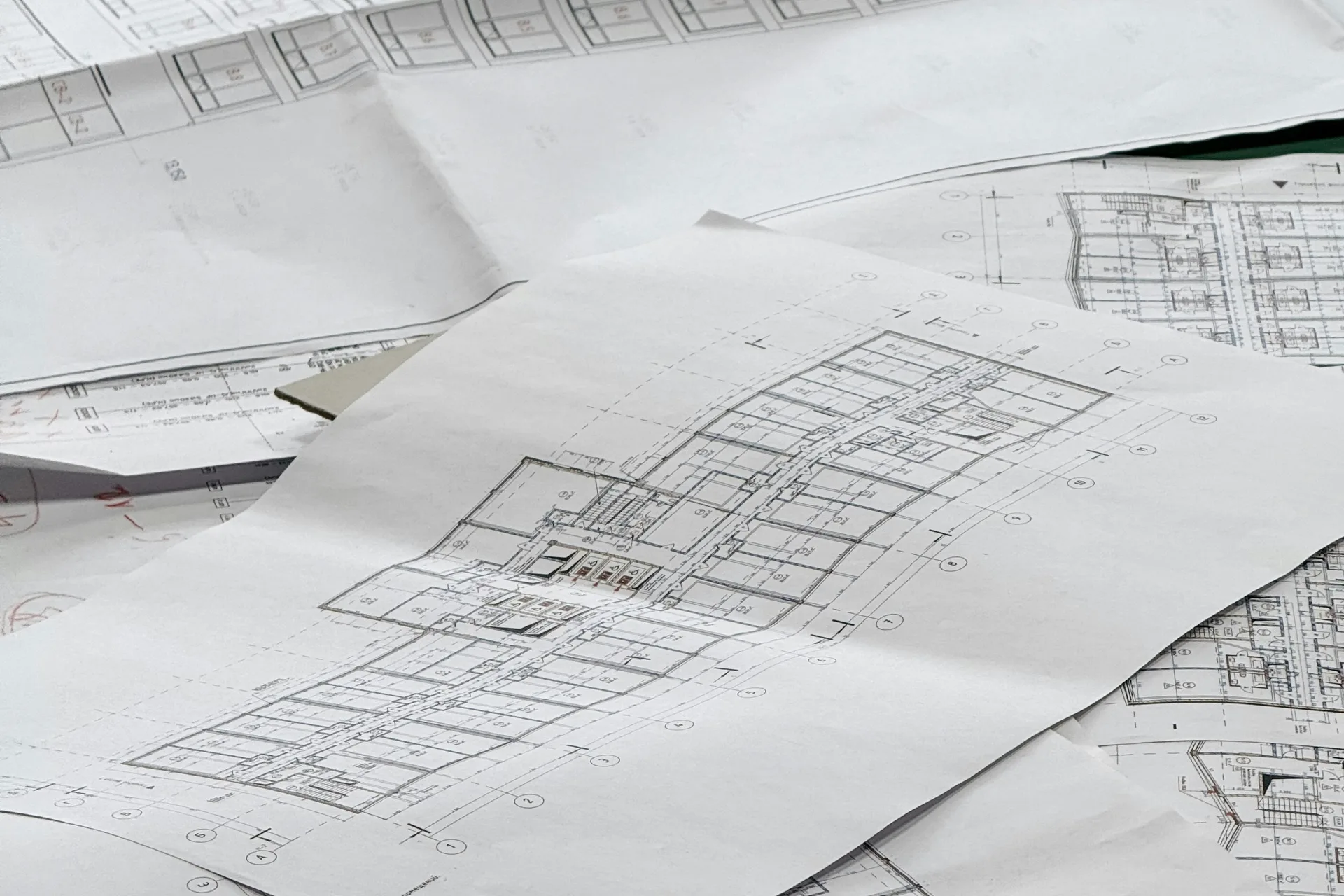 Architectural drawings spread out over a desk, the sheet in the middle open and showing a dimensioned floor plan.