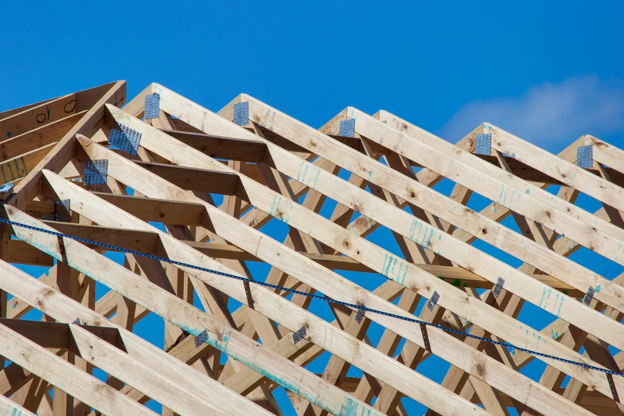 Prefabricated timber roof trusses standing in a row against a clear sky, their joints held by pressed metal plates.