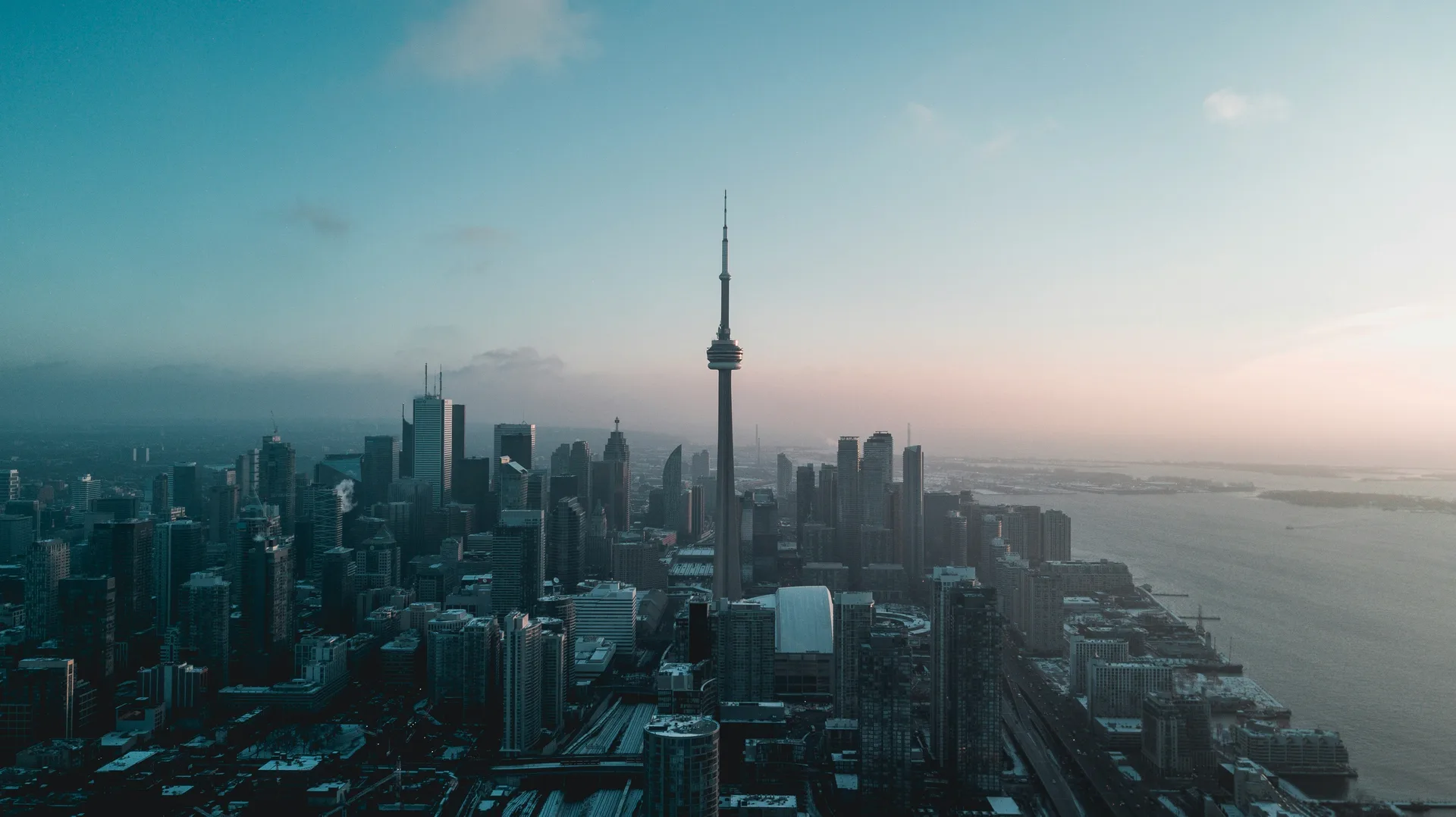 A city skyline from the air at dusk, office towers against a lake behind them.